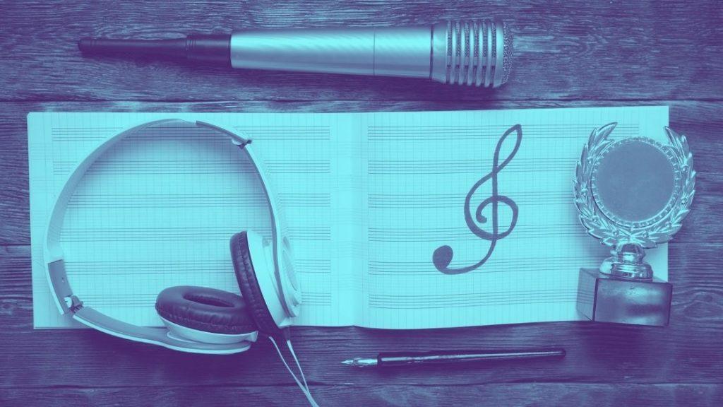 Miten menestyä musiikkialalla -artikkelikuva, nuottivihko, jossa vain piirretty nuottiavain, kuulokkeet, kynä mikrofoni ja palkintopysti